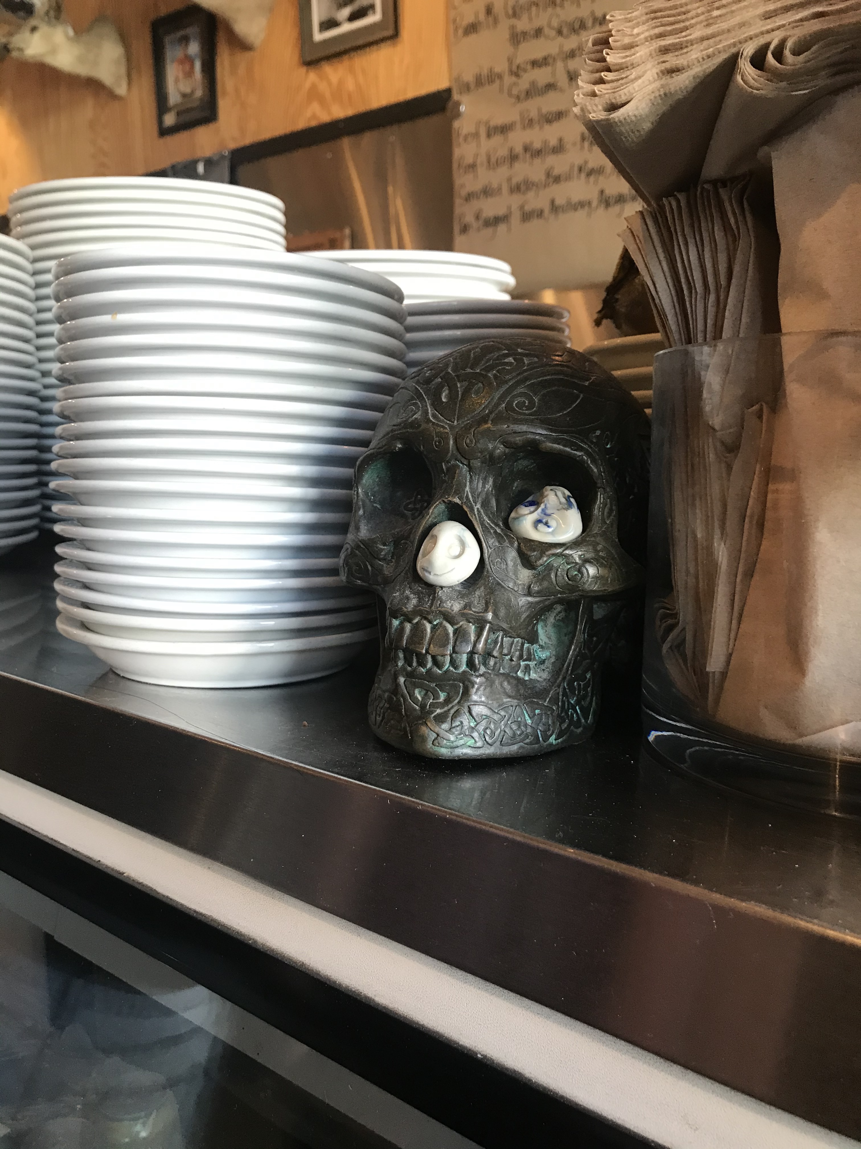 Interior picture of Industrial Eats, showing stacks of plates on the counter entrance and a patina skull.